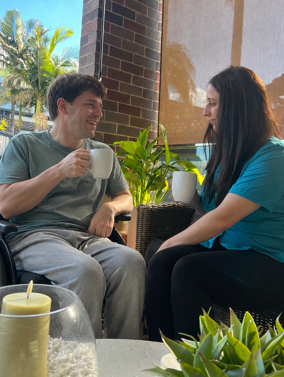 A NutureNest support worker and a man in a wheelchair sharing a cup of tea outdoors