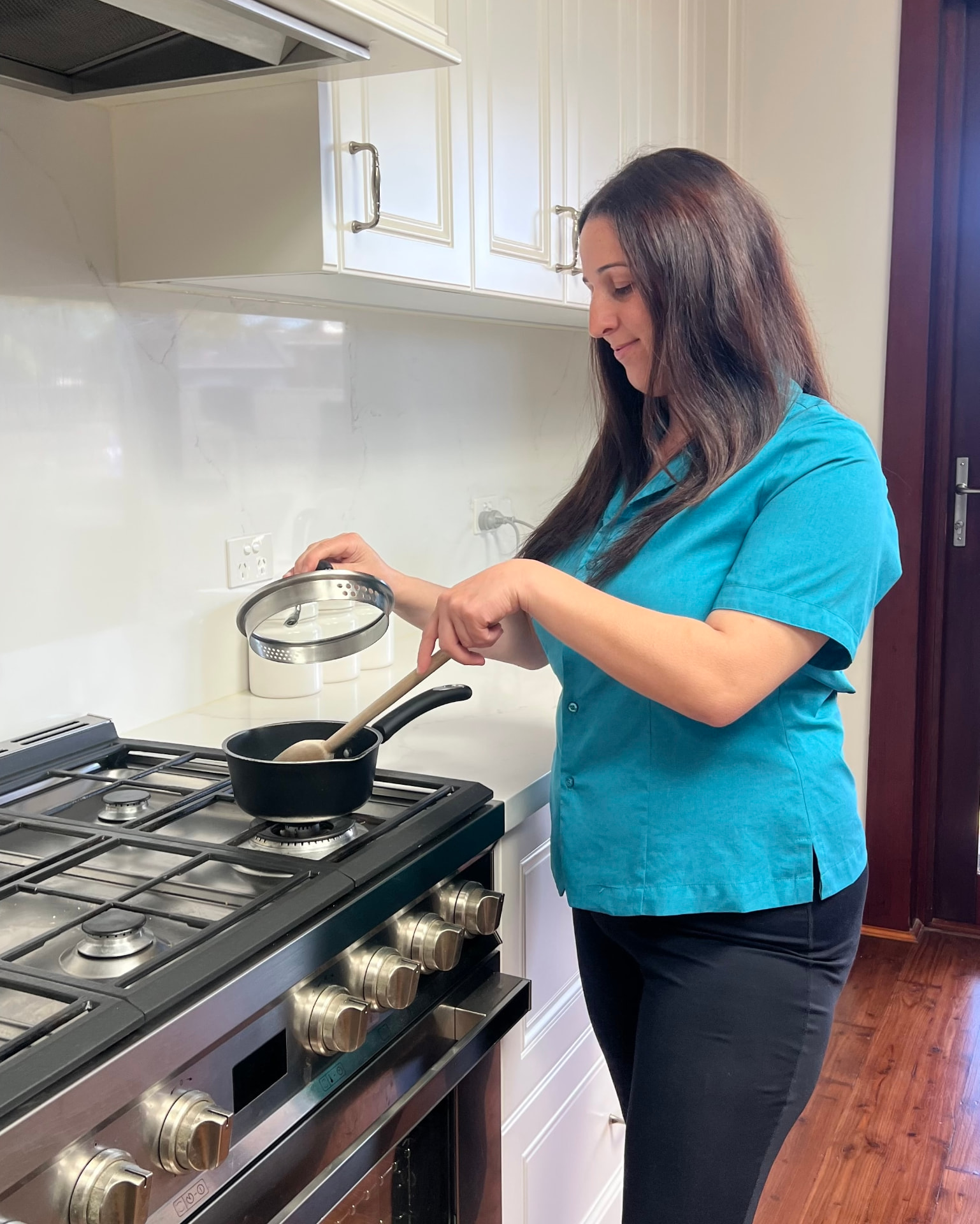 A NutureNest support worker checking a pot on the stove during a personal care visit