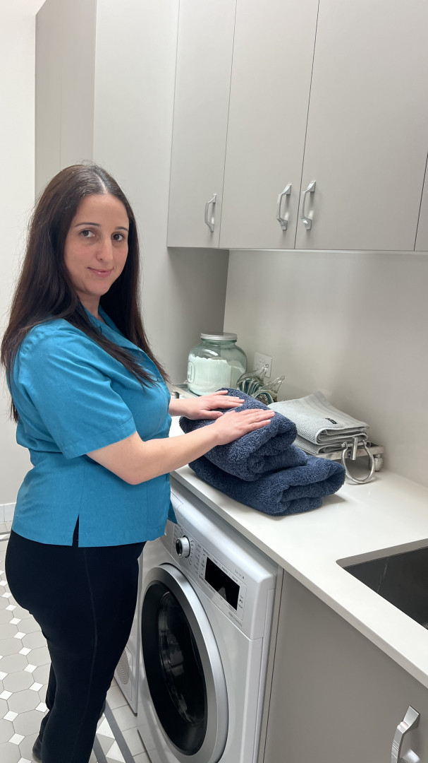 A NutureNest support worker folding fresh towels in a home laundry during a personal care visit in South West Sydney