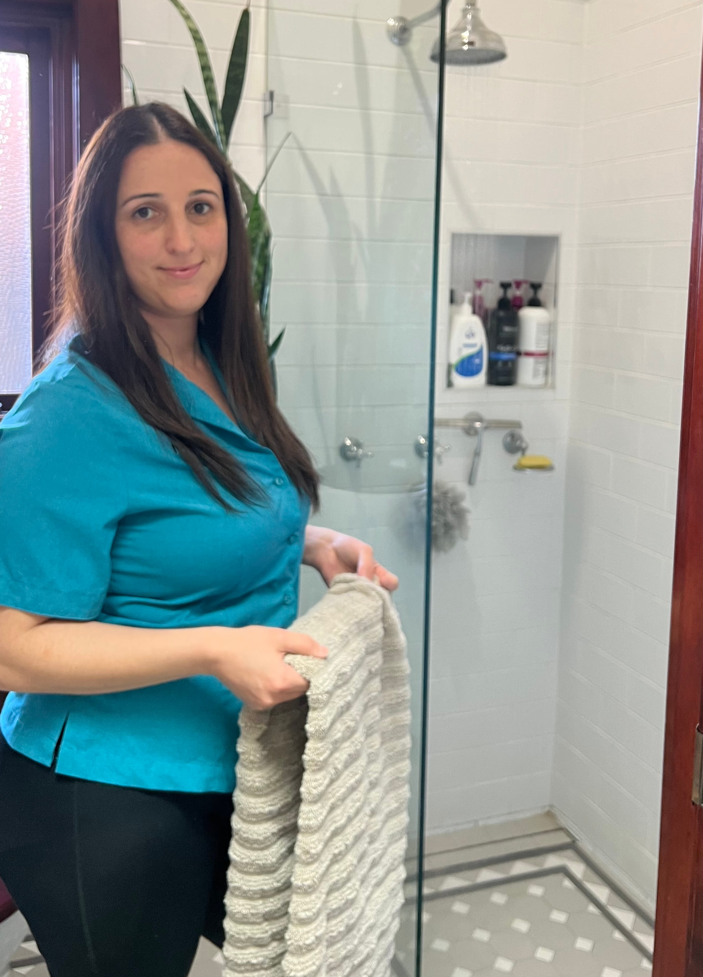 A NutureNest support worker hanging a fresh towel in a bathroom while setting up a domestic assistance routine
